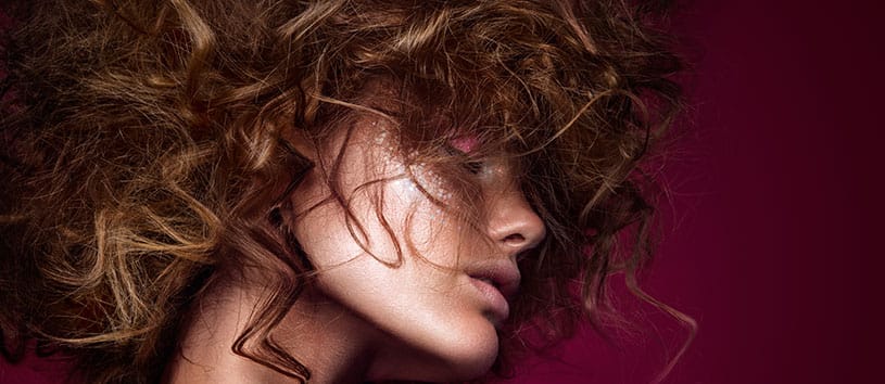 Side profile of woman with curly hair and bright makeup.