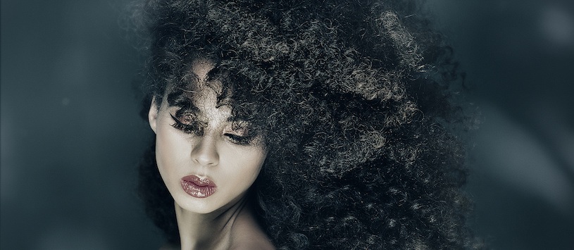 Woman with large, curly hair looking downwards.